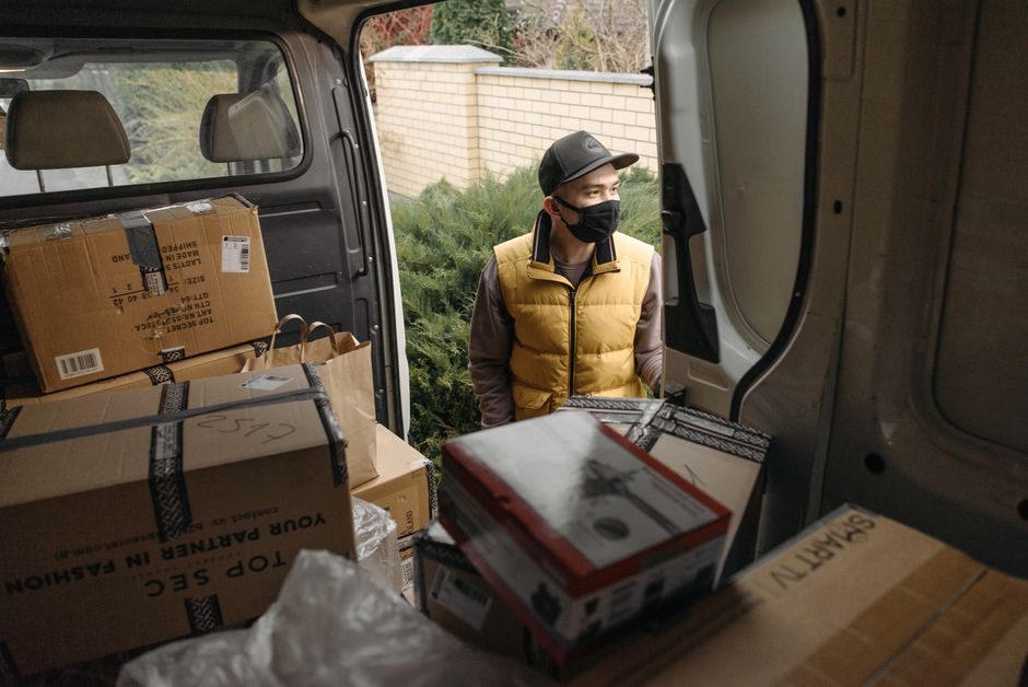 Courier in a mask loading packages into a van. Safe, modern logistics during new normal.